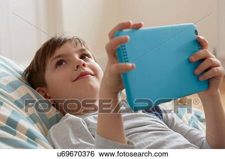 Boy reclining on beanbag chair looking up from digital tablet View Large Photo Image Stock Photograph - Boy reclining on beanbag chair looking up from digital tablet. Fotosearch