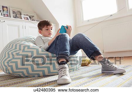 Boy reclining on beanbag chair looking at digital tablet View Large Photo Image Stock Photography - Boy reclining on beanbag chair looking at digital tablet. Fotosearch