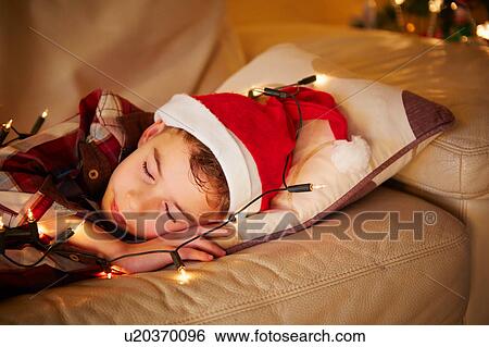 Boy sleeping, wearing santa hat and lights on sofa at christmas View Large Photo Image Stock Photograph - Boy sleeping, wearing santa hat and lights on sofa at christmas. Fotosearch