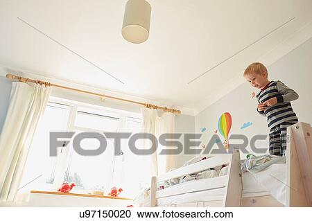 Stock Image - Boy standing on top of bunk bed. Fotosearch