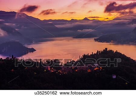 Stock Image - Cloud covered mountains across Lake Como at sunset, Varenna, Italy. Fotosearch