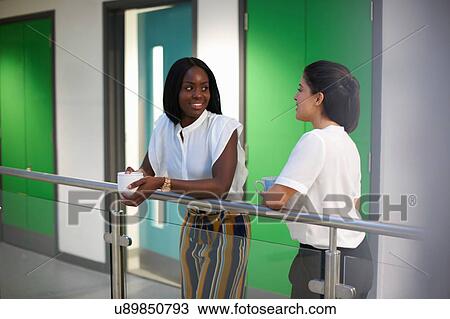 Stock Image - Colleagues chatting in office building. Fotosearch