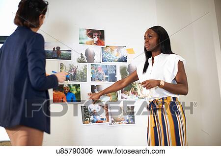 Stock Photograph - Colleagues in office discussing photographs on wall. Fotosearch