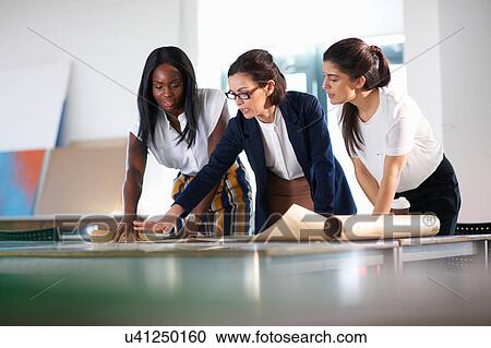 Stock Image - Colleagues in office looking at blueprint. Fotosearch