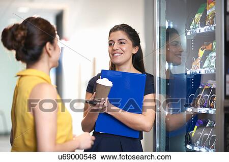 Stock Photo - Colleagues using vending machine chatting. Fotosearch