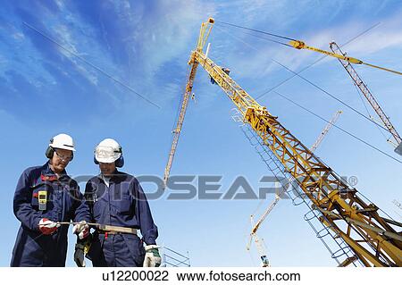 Stock Image - Construction workers on site with cranes. Fotosearch