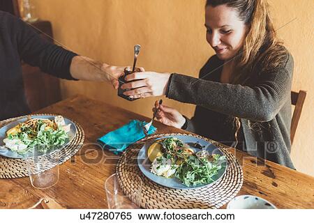 Stock Photography - Couple handing jar over lunch table. Fotosearch