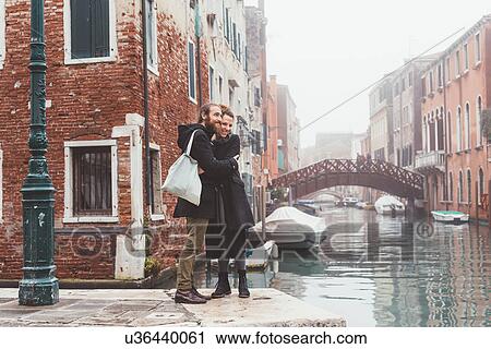 Stock Image - Couple hugging on misty canal waterfront, Venice, Italy. Fotosearch