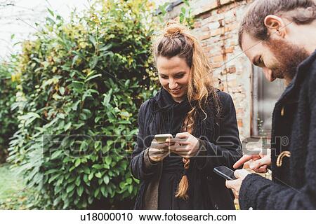 Stock Image - Couple in garden looking at smartphones. Fotosearch