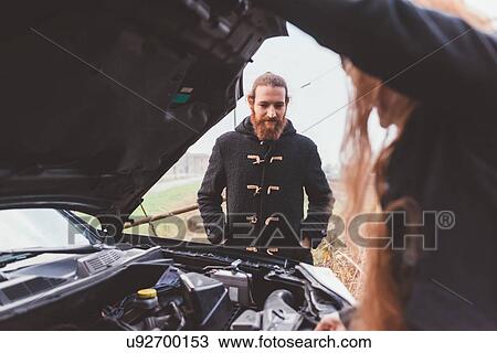 Stock Image - Couple looking at car engine on roadside. Fotosearch