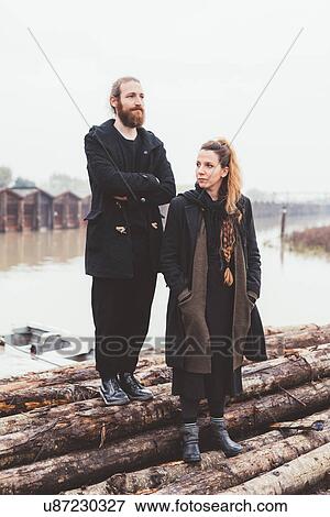 Stock Photo - Couple on logs at misty canal waterfront. Fotosearch