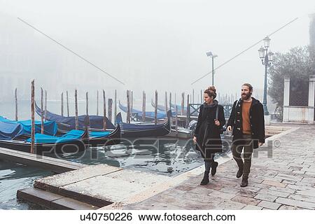 Stock Photograph - Couple strolling along misty canal waterfront, Venice, Italy. Fotosearch