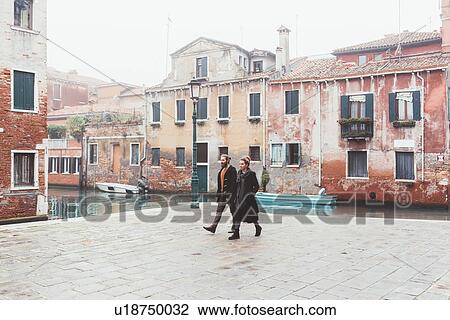 Stock Image - Couple strolling by canal waterfront, Venice, Italy. Fotosearch