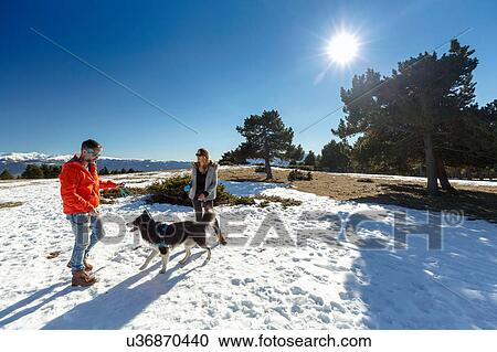 Stock Image - Couple with dog in snow covered landscape. Fotosearch