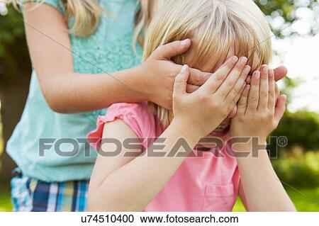Stock Image - Cropped shot of girl with hands covering friend's eyes in garden. Fotosearch