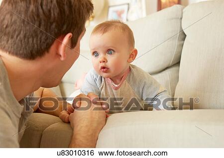 Stock Photograph - Cute blue eyed baby girl on sofa staring at her father. Fotosearch