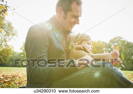 Daughter sitting on father's lap holding autumn leaf View Large Photo Image Stock Image - Daughter sitting on father's lap holding autumn leaf. Fotosearch