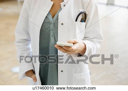 Stock Image - Doctor holding smartphone, mid section. Fotosearch
