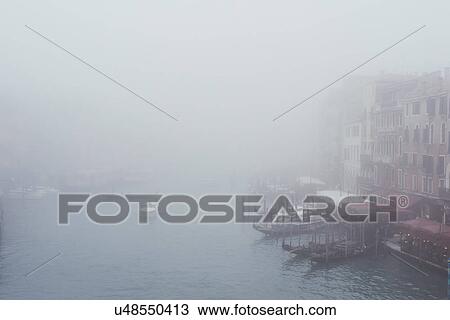 Stock Image - Elevated view of misty canal waterfront, Venice, Italy. Fotosearch