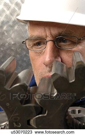 Engineer scrutinising metal cogs View Large Photo Image Stock Image - Engineer scrutinising metal cogs. Fotosearch