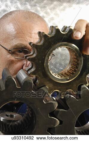 Stock Image - Engineer scrutinising metal cogs. Fotosearch