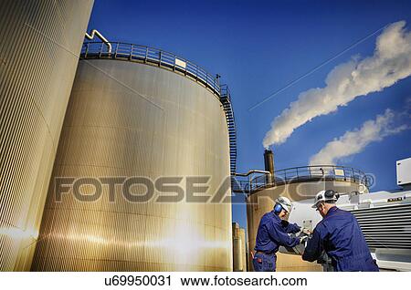 Stock Image - Engineers by oil storage towers. Fotosearch