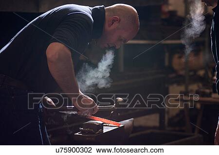 Stock Image - Farrier forging horseshoe on anvil. Fotosearch