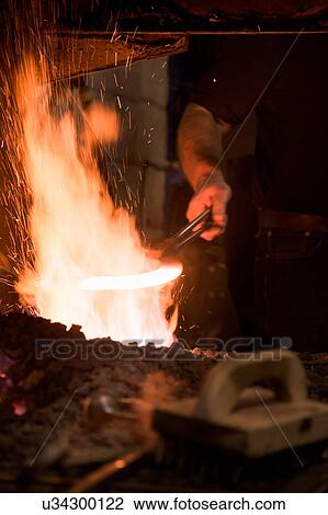 Stock Image - Farrier heating metal for horseshoe in fire. Fotosearch