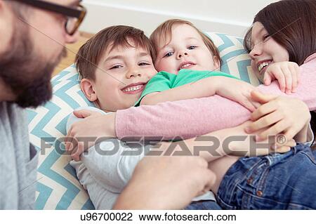 Stock Image - Father and three smiling children reclining on beanbag chair. Fotosearch