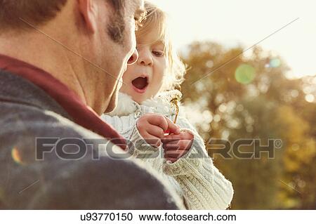 Stock Image - Father carrying daughter holding dandelion clock. Fotosearch