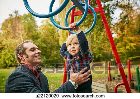 Stock Image - Father helping daughter on monkey bars in playground. Fotosearch
