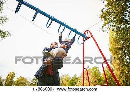 Stock Photo - Father helping daughter on monkey bars in playground. Fotosearch