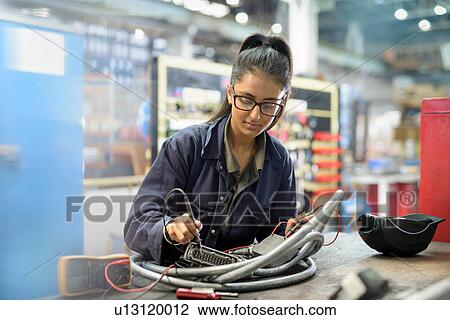 Stock Image - Female apprentice electrician in car factory. Fotosearch