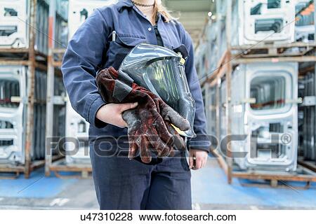 Stock Photo - Female apprentice welder holding equipment in car factory. Fotosearch