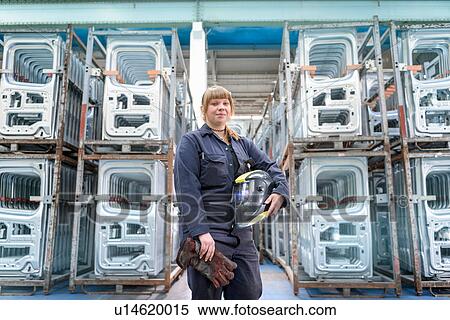 Stock Photography - Female apprentice welder holding equipment in car factory, portrait. Fotosearch