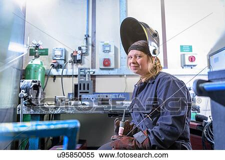 Stock Photography - Female apprentice welder holding equipment in car factory, portrait. Fotosearch
