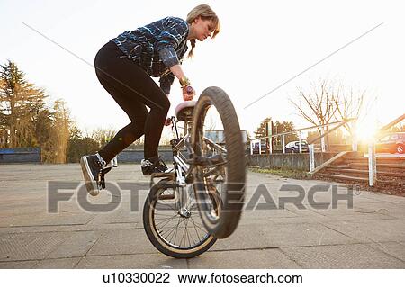 Stock Image - Female BMX rider doing BMX trick in park. Fotosearch