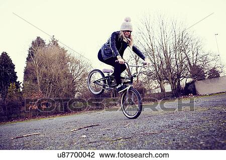 Stock Image - Female BMX rider doing BMX trick on wasteland. Fotosearch