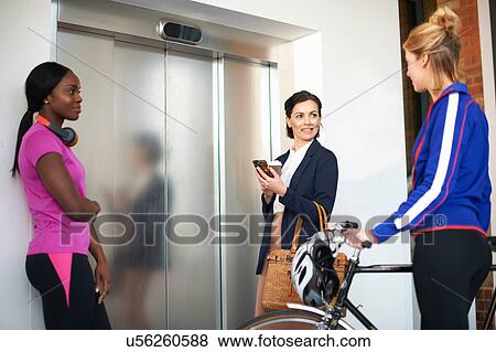 Stock Photo - Female colleagues waiting for office lift. Fotosearch