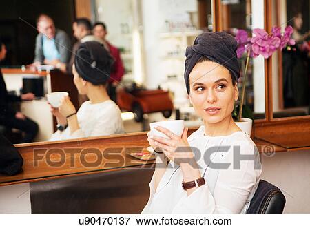 Stock Photo - Female customer with towel around hair and coffee cup in hair salon. Fotosearch