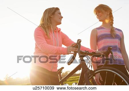 Stock Photo - Female cyclists strolling with racing cycle in sunlit park. Fotosearch