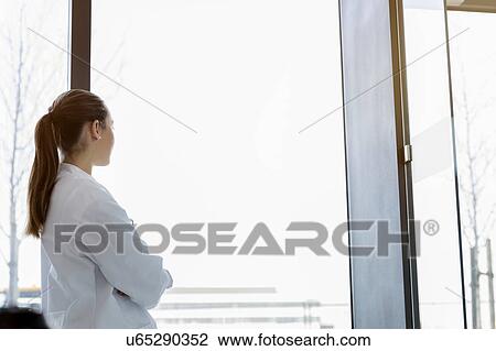 Stock Image - Female doctor looking out of window, rear view. Fotosearch