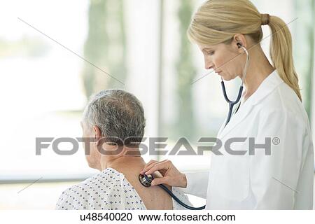 Stock Image - Female doctor using stethoscope on male patient. Fotosearch