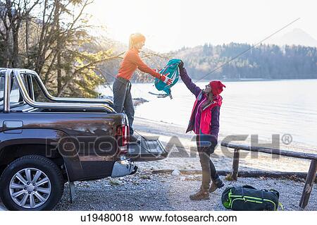 Stock Photo - Female hiker handing backpack to friend on lakeside in Bavarian Alps. Fotosearch