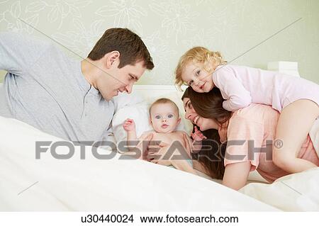 Picture - Female toddler and baby sister playing in bed with parents. Fotosearch