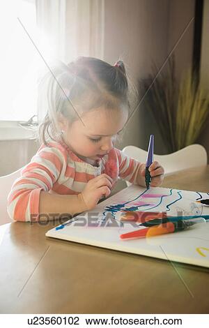 Stock Image - Female toddler at table drawing in sketchbook. Fotosearch