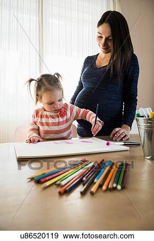 Female toddler at table with pregnant mother drawing in sketchbook View Large Photo Image Stock Photo - Female toddler at table with pregnant mother drawing in sketchbook. Fotosearch
