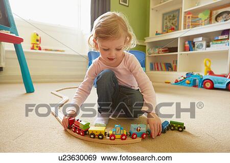 Stock Photo - Female toddler playing with toy train on playroom floor. Fotosearch