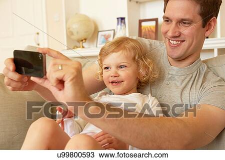 Female toddler sitting on father's knee taking smartphone selfie View Large Photo Image Stock Image - Female toddler sitting on father's knee taking smartphone selfie. Fotosearch