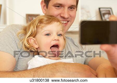 Female toddler sitting on father's knee sticking out tongue for smartphone selfie View Large Photo Image Stock Photo - Female toddler sitting on father's knee sticking out tongue for smartphone selfie. Fotosearch
